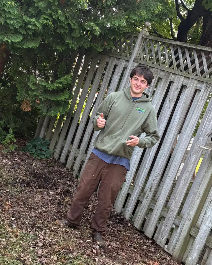 Weston Scalise, co-owner of EdmisonH&P Property Maintenance, giving a thumbs up beside a cleared fence line after a yard cleanup